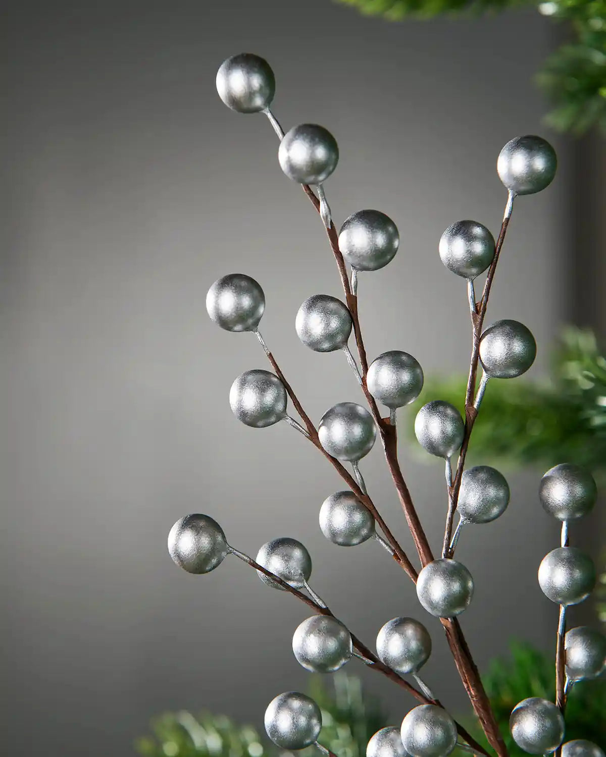 Close up of Decorative branch with silver berries on a Christmas tree against a grey blurry background
