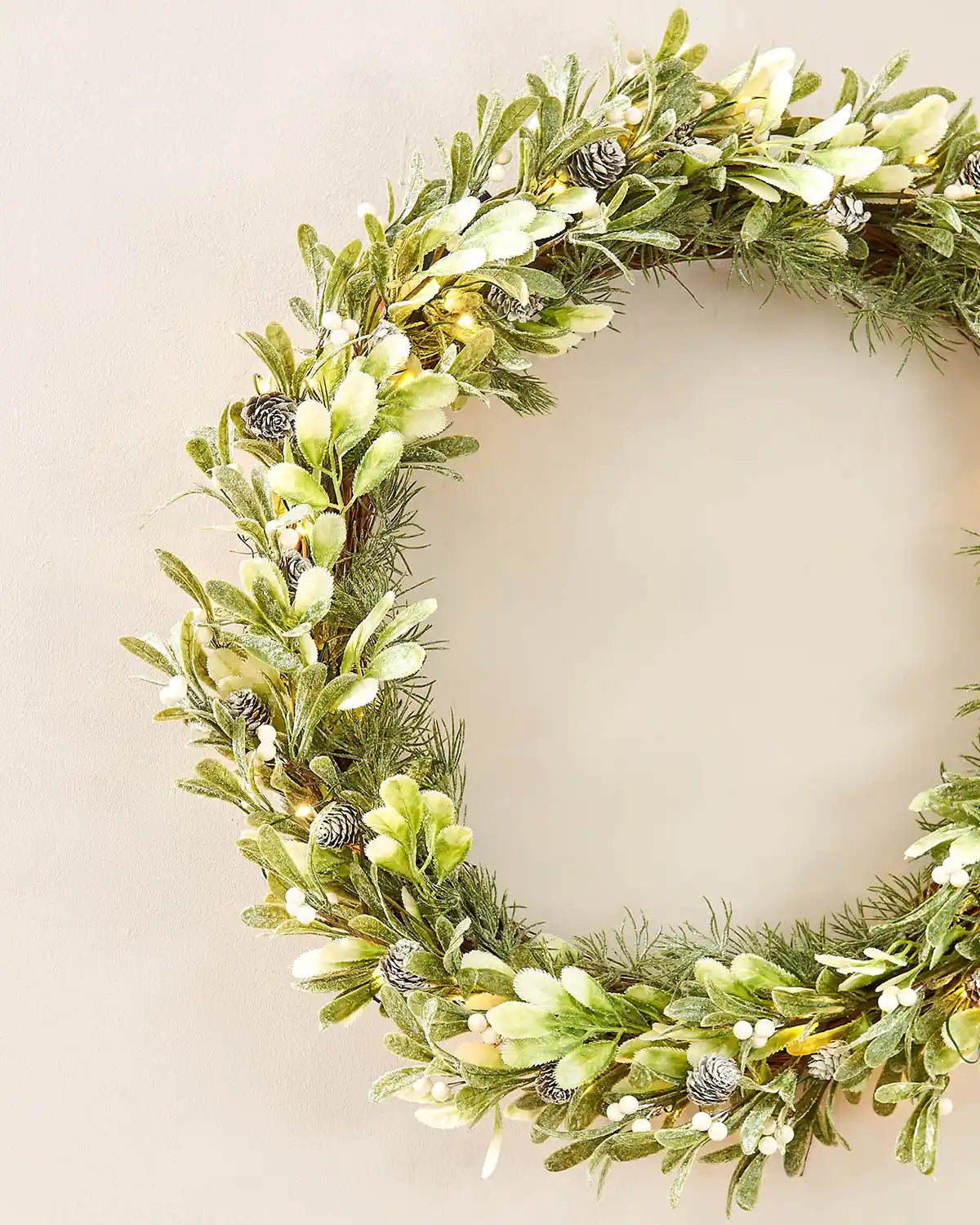 Close up of Decorative wreath with greenery and small white flowers on a Beige background