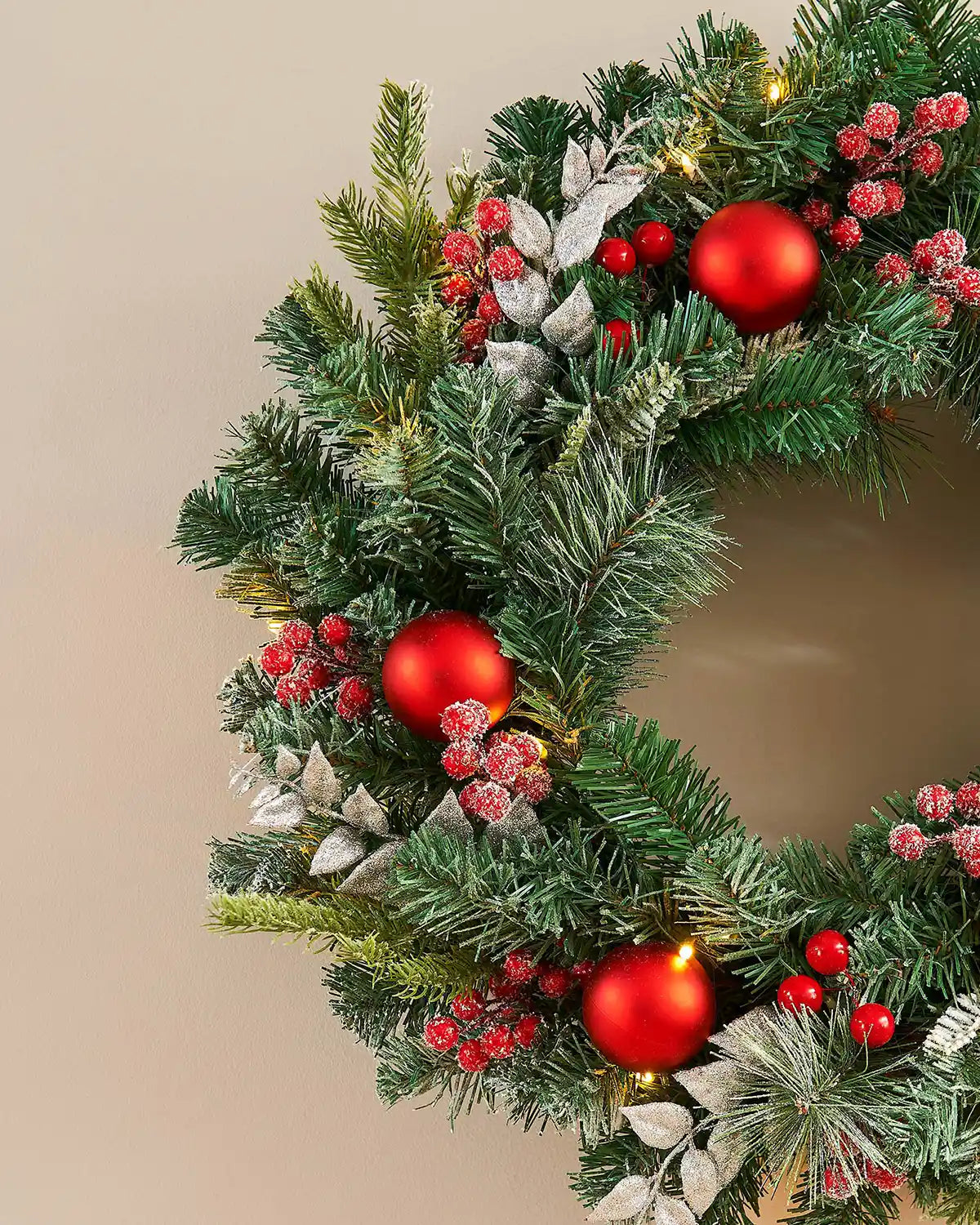 Close up of Frosted Christmas wreath with red berries and lights on a white background on a beige background