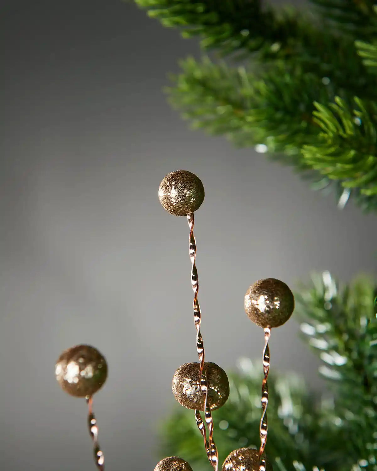 Close up of Gold Glitter Berry Christmas Tree Spray on a grey background