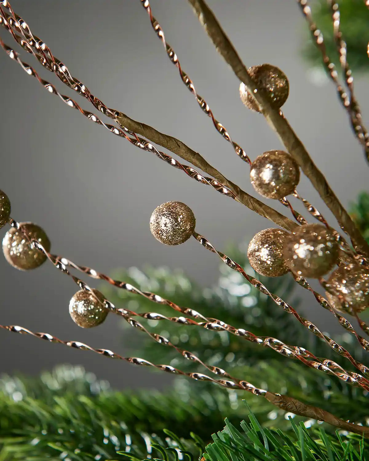 Close up of Gold Glitter Berry Christmas Tree Spray on a grey background and a Christmas tree
