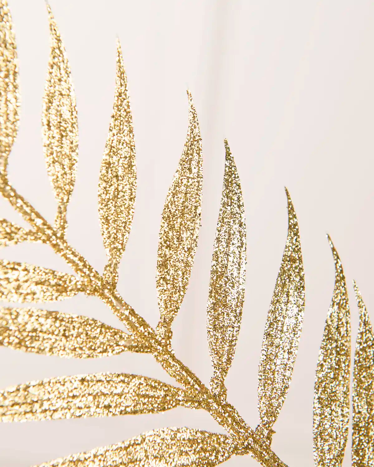 Close up of Gold glitter Fern Leaf Christmas Tree Spray leaves showing the gold glitter leaf details with a blurry cream background