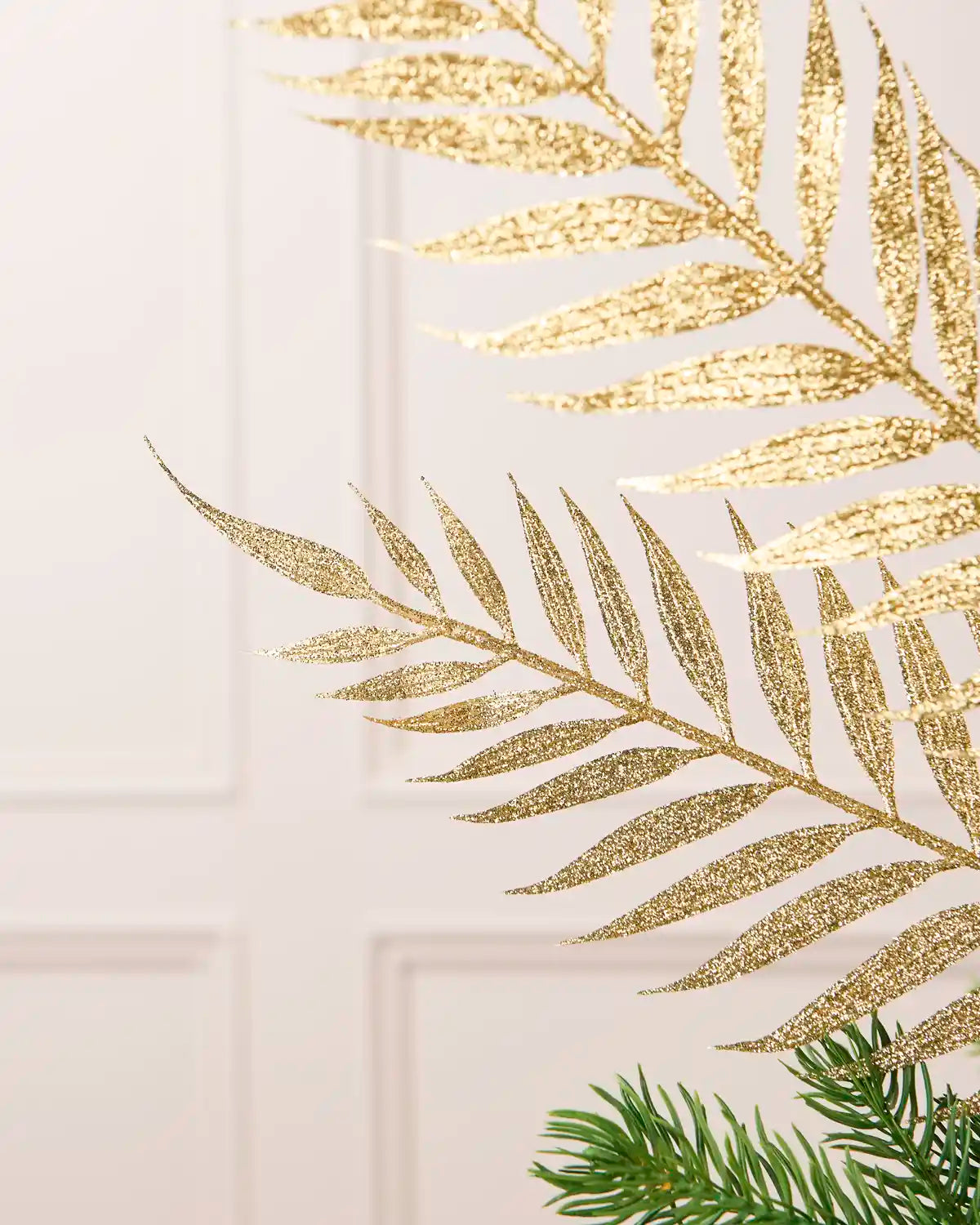 Close up of Gold glitter Fern Leaf Christmas Tree Spray leaves showing the gold stem and gold leaves with a blurry cream background