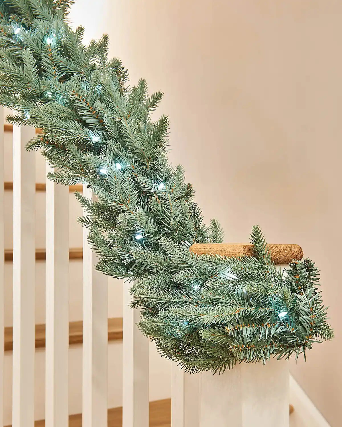 Close up of Green garland with Ice white lights on a staircase banister against a cream wall