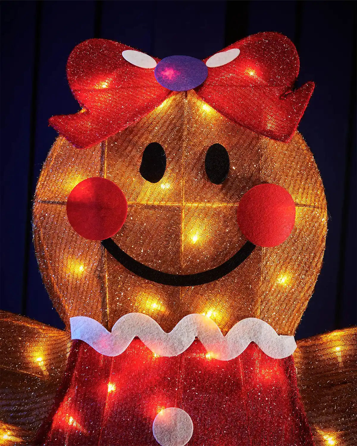 Close up of LED gingerbread lady with a red bow and lights against a dark background