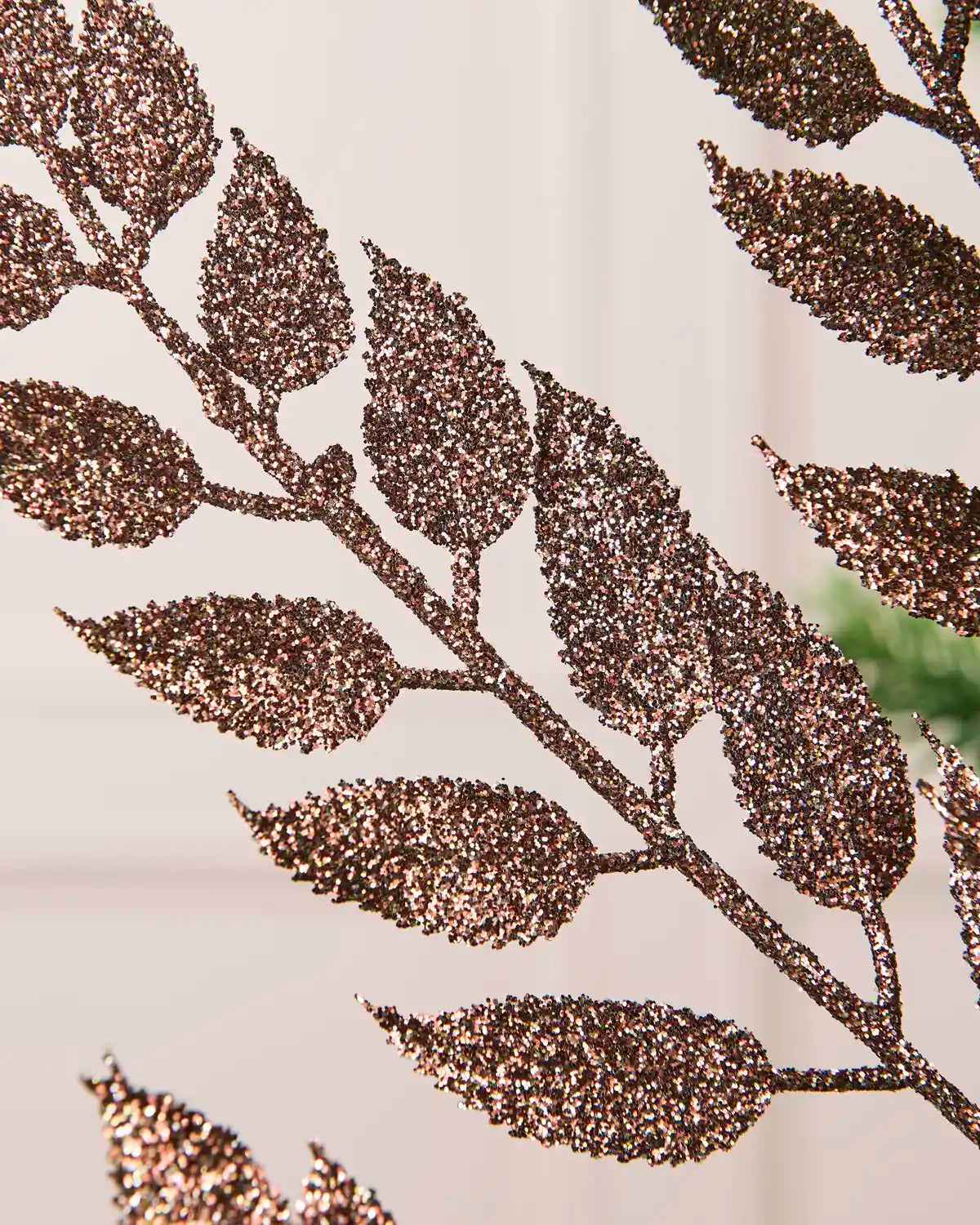 Close up of Mocha Leaf Christmas Tree spray leaves coated in glitter with a blurry cream background. 