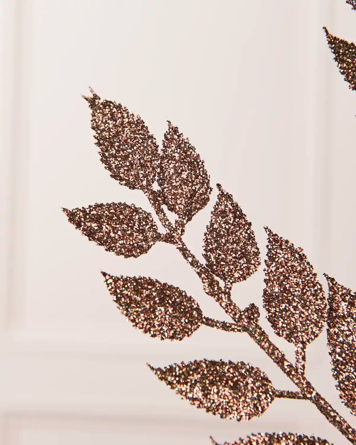 Close up of Mocha Leaf Christmas Tree spray leaves coated in glitter and a blurry cream background