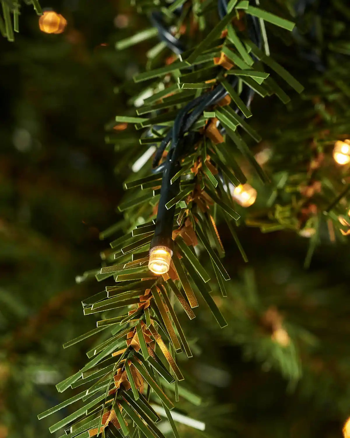 Close up of PVC and PE tips with single lit warm white bulbs on a 7ft Christmas tree