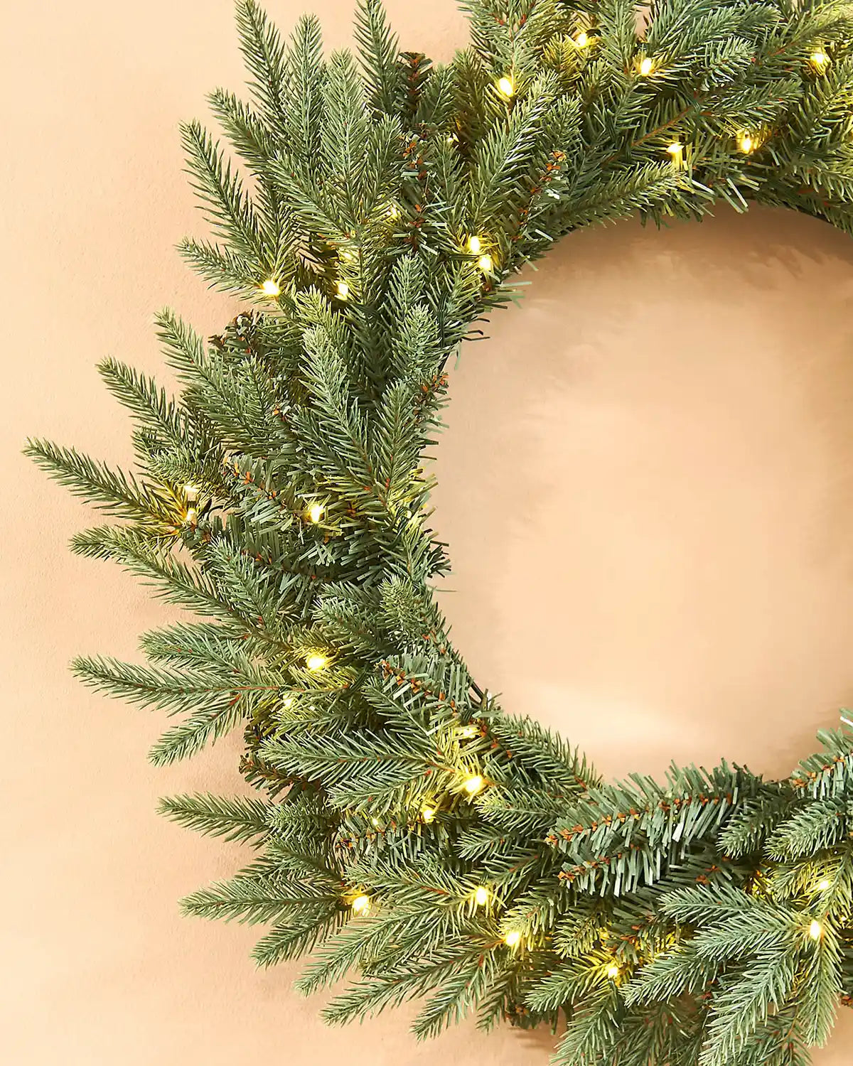 Close up of Pre-Lit Blue Mixed Pine Wreath, 60 cm with warm white lights on a cream wall