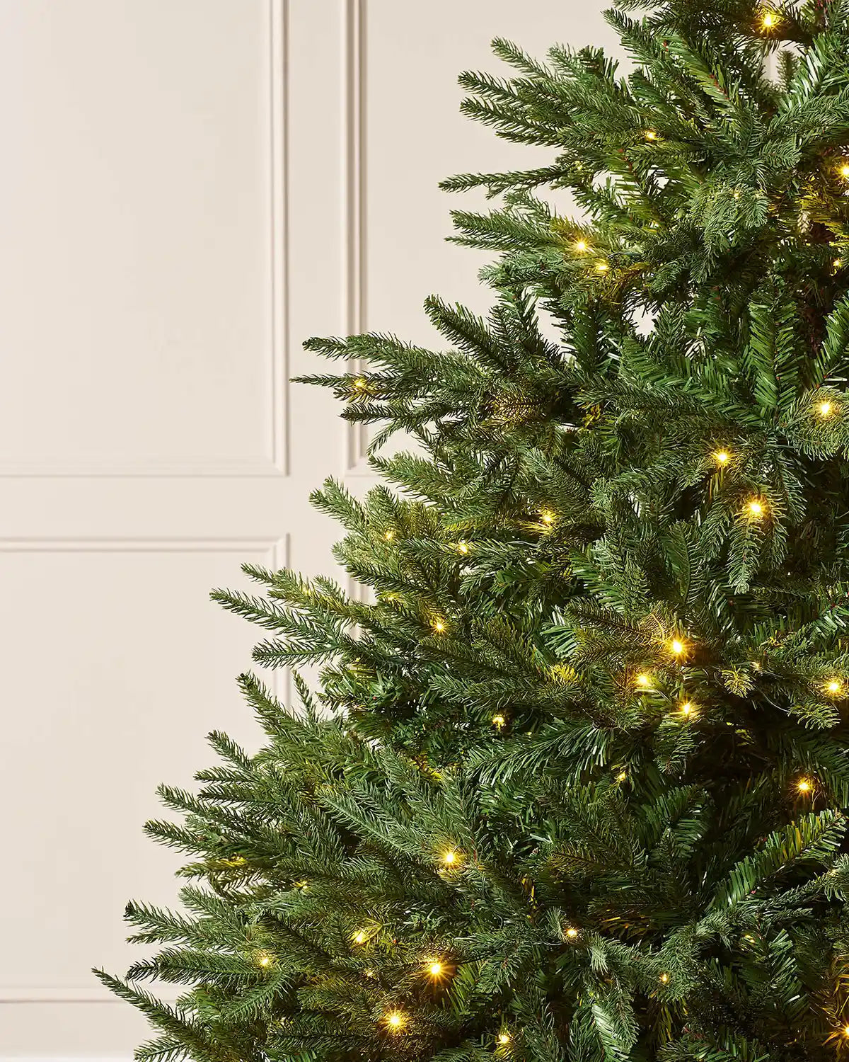 Close up of Pre-Lit Nordmann Fir Christmas Tree, 7 ft on against a cream panel wall