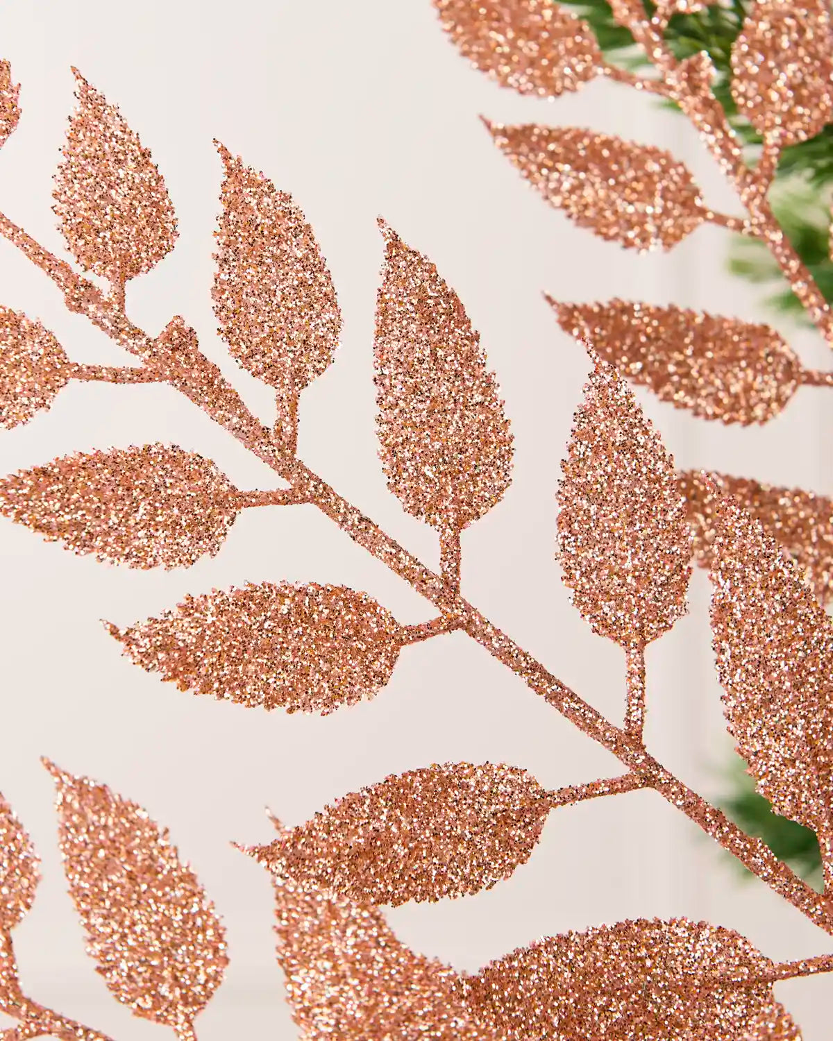Close up of Rose Gold Leaf Christmas Tree Spray coated in rose gold glitter and a blurry cream background. 