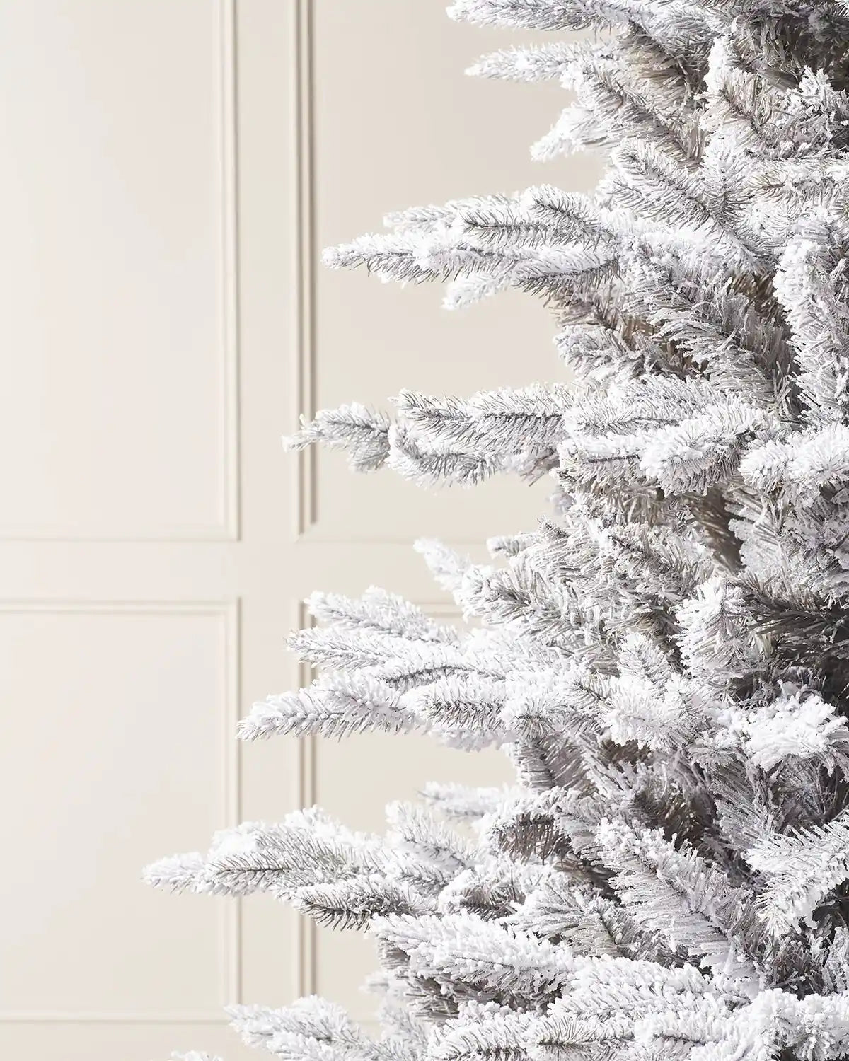 Close up of Snow flocked Christmas tree on with against a cream Panel wall