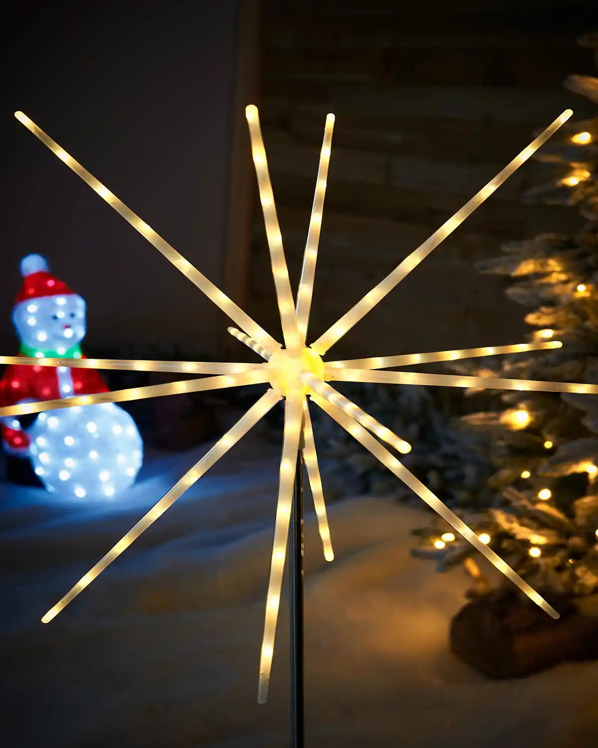 Close up of Starburst Pathway Stake Light, Warm White, 98 cm featuring 14 light tubes in a garden with Christmas tree and Snowman figurine 