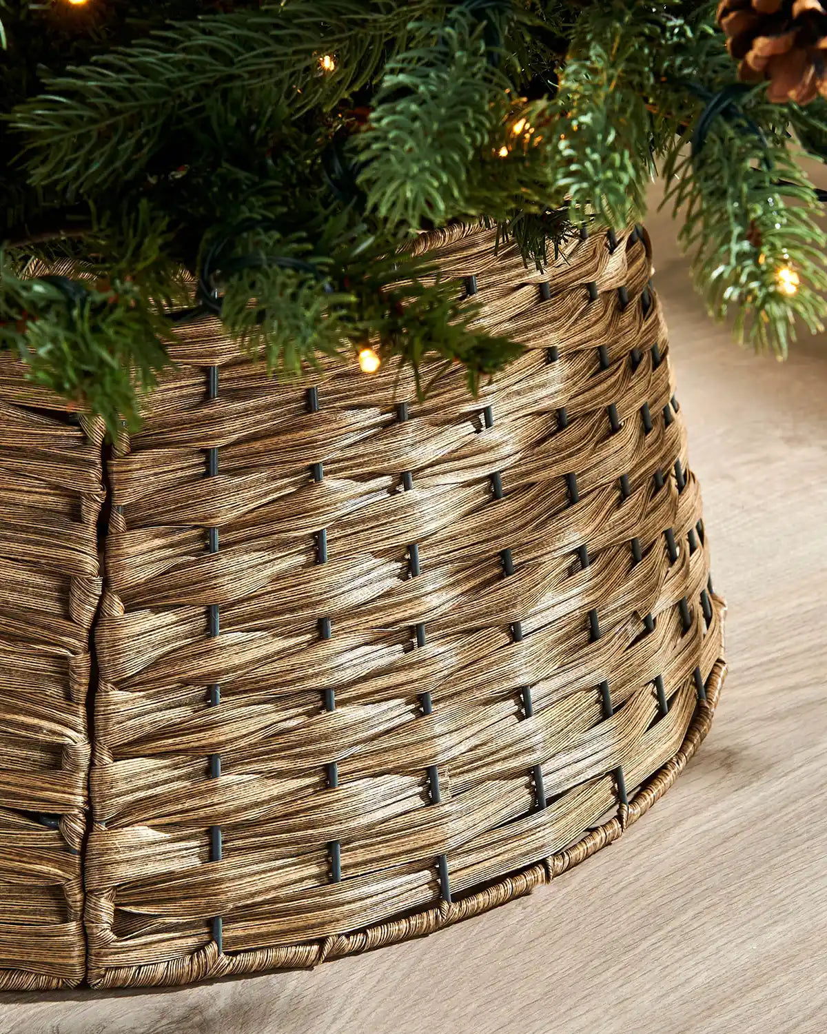 Close up of a Brown rattan Christmas tree skirt with a decorated tree on a wooden floor