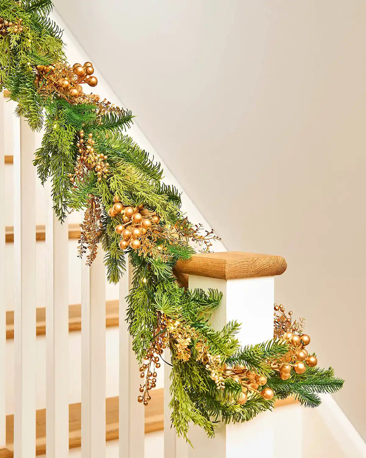 Close up of a Decorative Christmas garland with gold berries on a staircase with a cream wall 