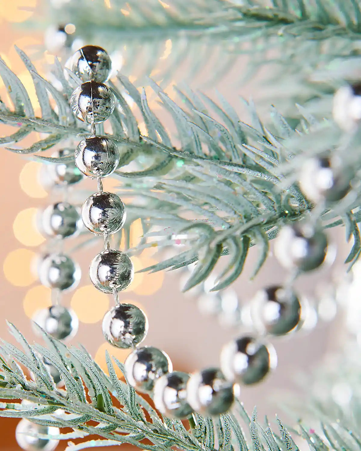 Close up of a Silver bead garland on a Christmas tree branch with a blurred lights background