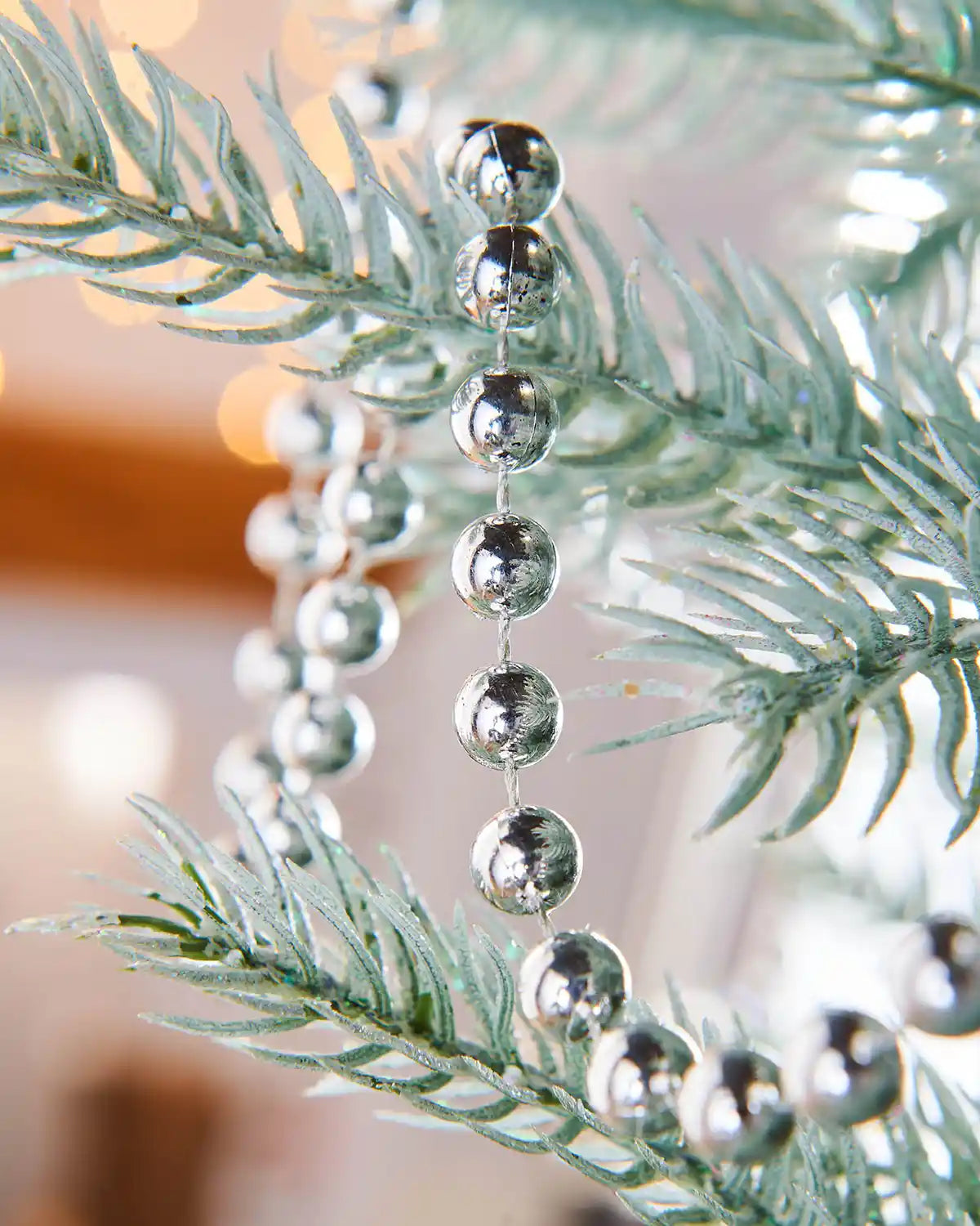 Close up of a Silver bead garland on a frosted Christmas tree branch with a blurred lights background