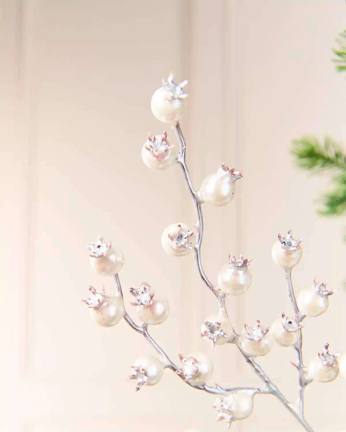 Close up of a Silver decorative pick with faux pomegranate ornaments, featuring large white pearl-like spheres and small silver crown details, set against a soft beige background.