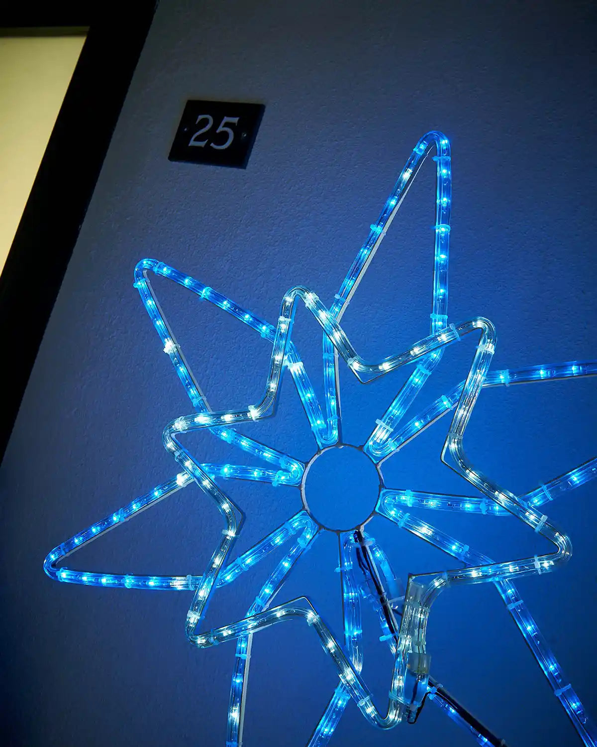 Close up of a White and blue LED lights in the shape of the Northern star silhouette on a dark blue garden wall