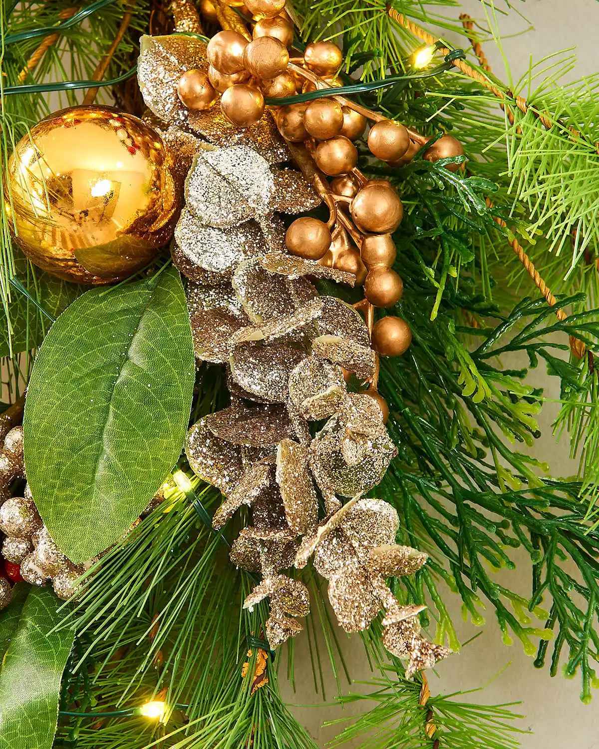 Close up of a decorative Christmas wreath with gold bauble, pinecones, and greenery on a light background