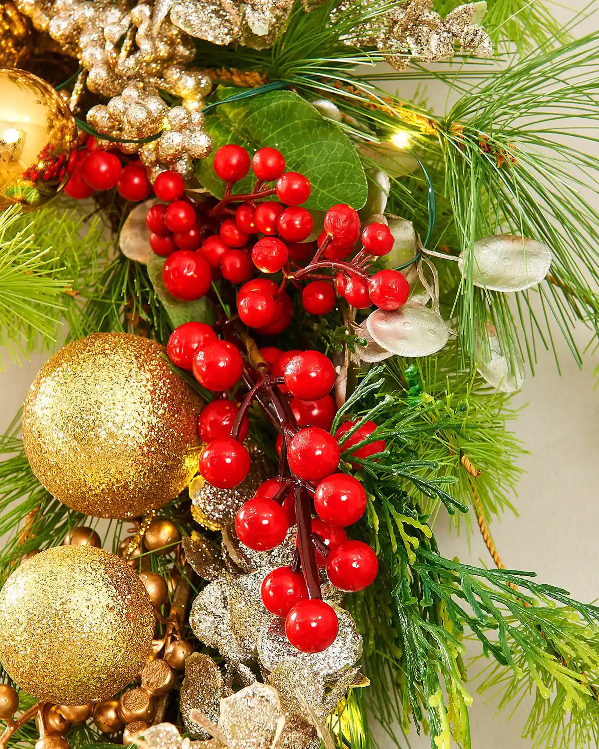Close up of a decorative Christmas wreath with gold ornaments, red berries, and green foliage.