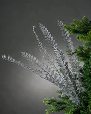 Close up of a decorative silver glitter branch with small leaves on a Christmas tree branch