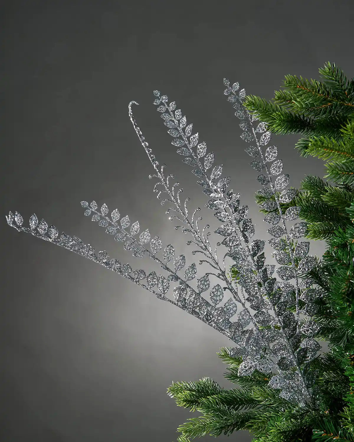 Close up of a decorative silver glitter branch with small leaves on a Christmas tree branch