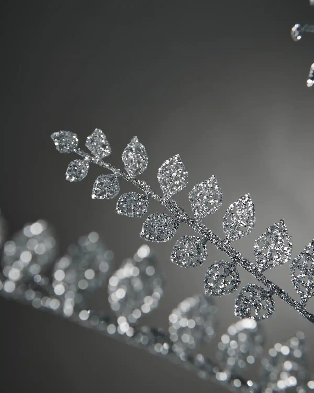 Close up of a decorative silver glitter branch with small leaves on a grey background