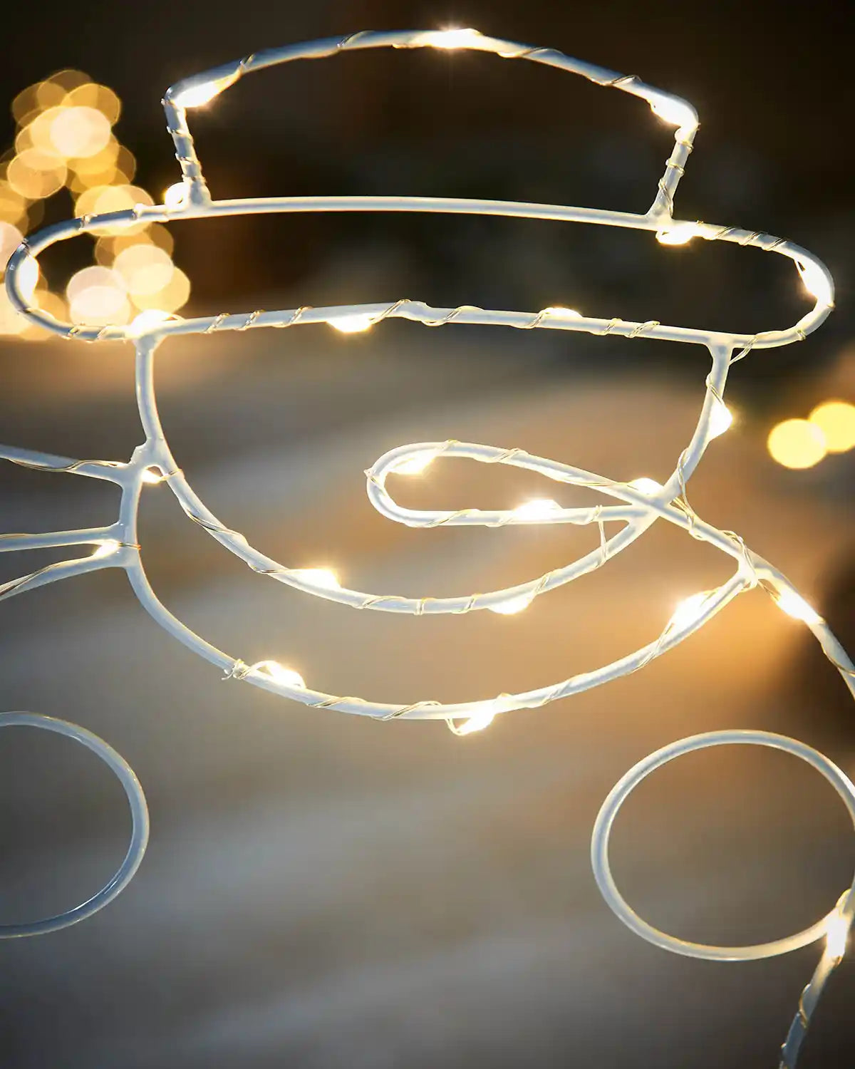 Close up of a decorative wire snowman face with carrot nose in warm white string lights against a snowy background