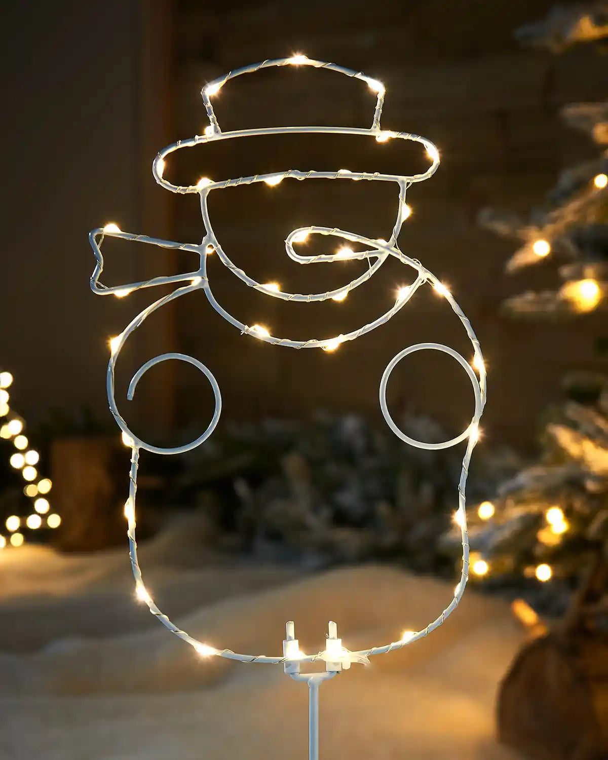 Close up of a decorative wire snowman with string lights against a snowy background