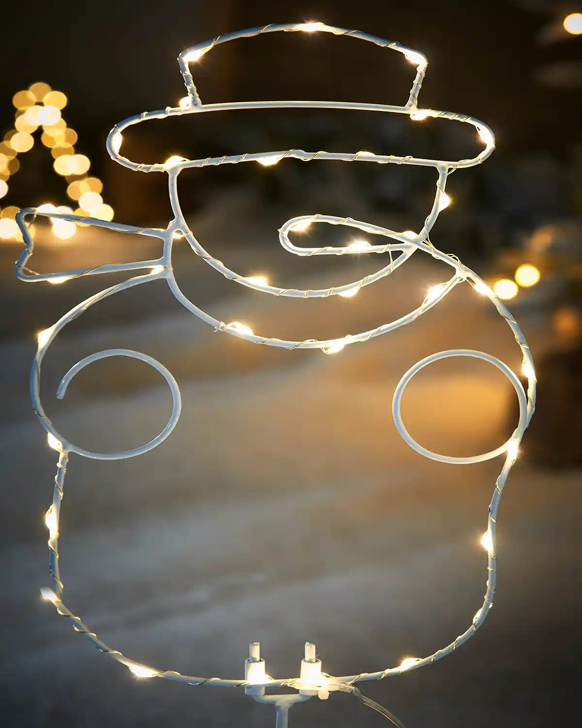 Close up of a decorative wire snowman with string lights against a snowy background