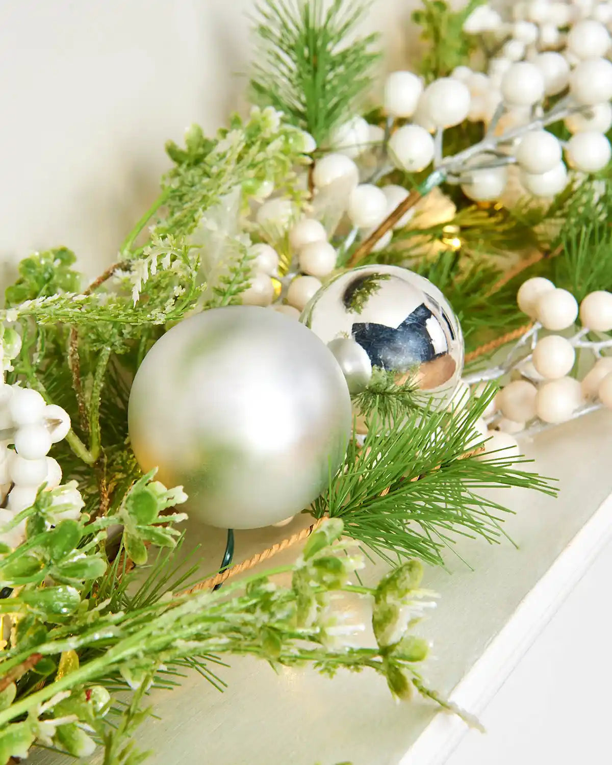 Close up of a garland with Silver Matt and gloss baubles along with white berries on a fireplace mantle 