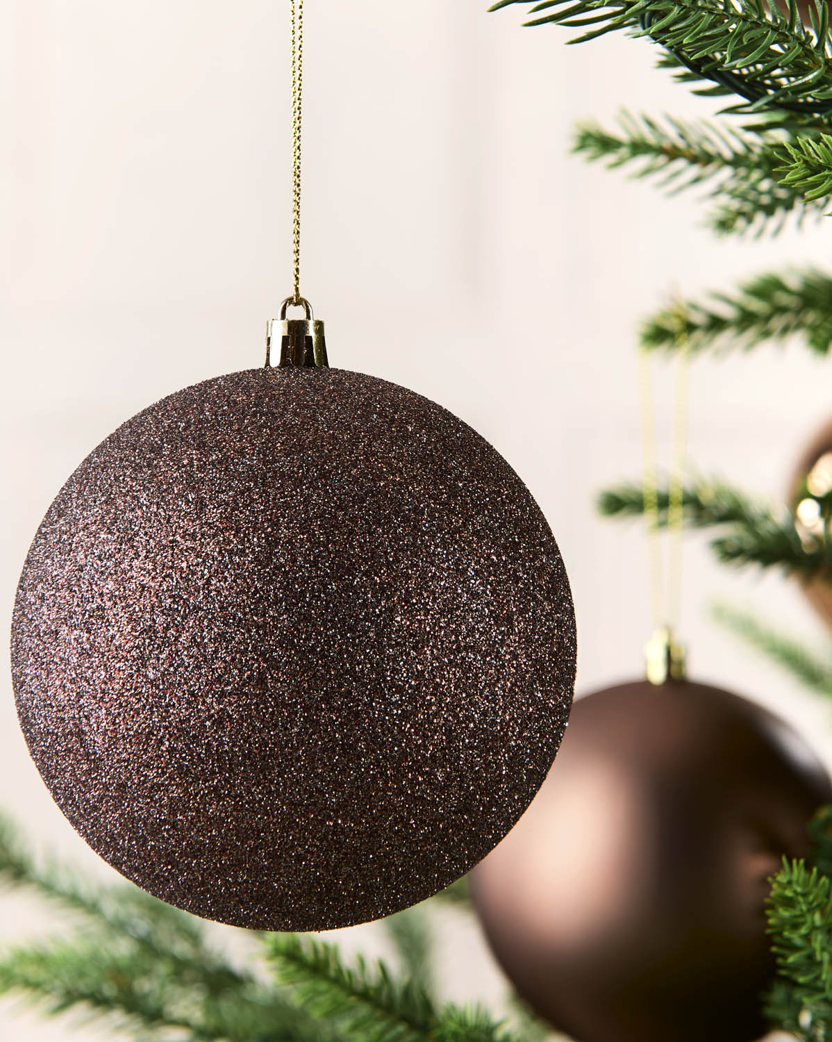 Close up of a glittery Espresso finishes hanging from the green branches of a Christmas tree.