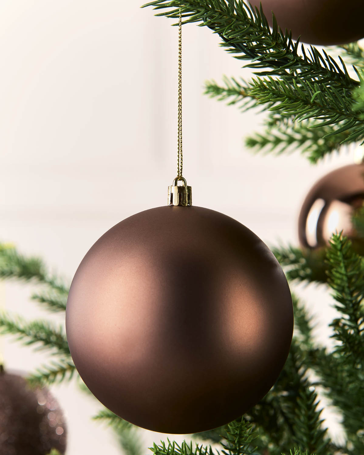 Close up of a matt espresso bauble on a Christmas tree against a blurry background