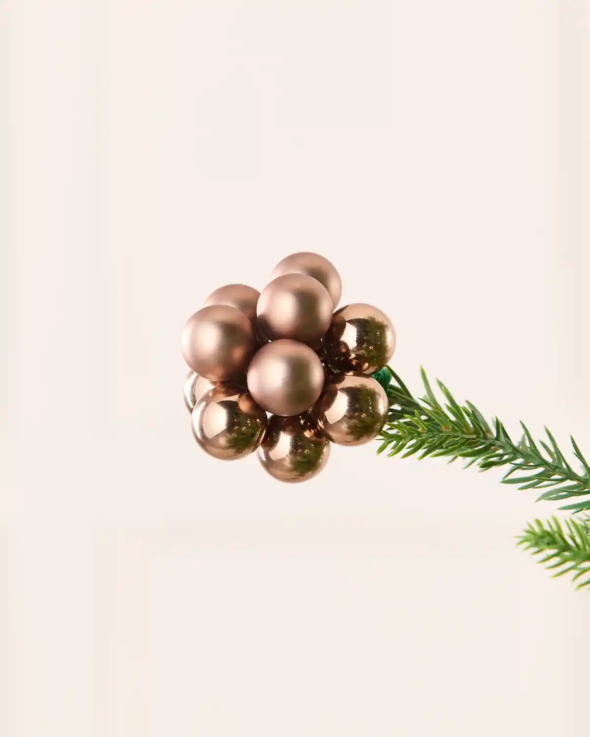Close up of a mocha bauble cluster on a Christmas tree branch against a cream background
