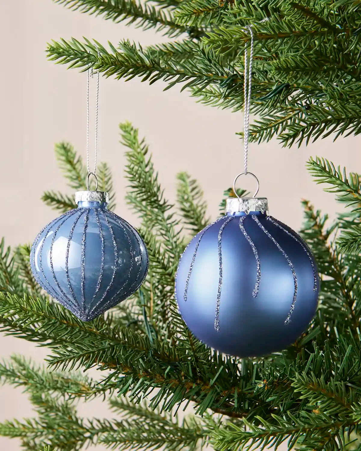 Close up of a onion and round shaped Ice blue glass bauble with glitter detailing, hanging from a Christmas tree branch