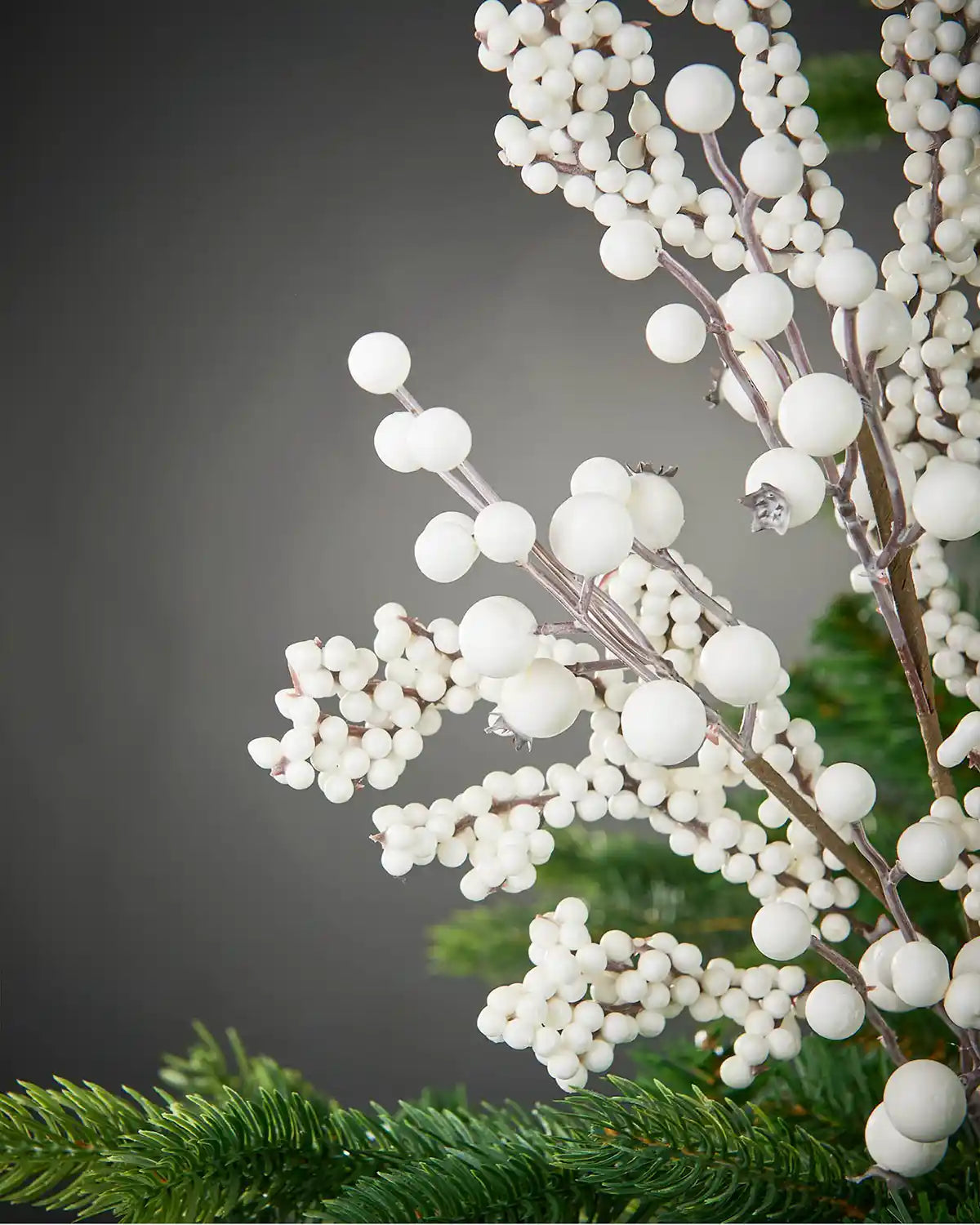 Close up of a white berry cluster branch on a Christmas tree against a grey background