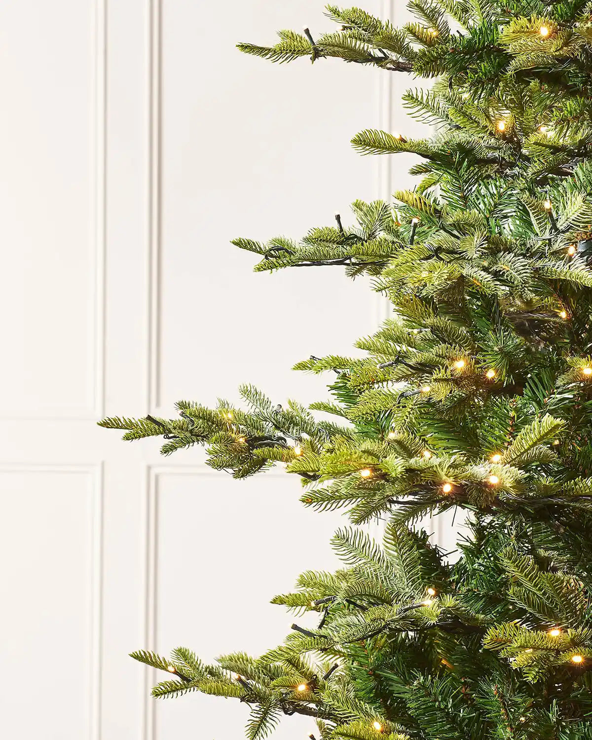 Close up of an 8ft Christmas tree with PVC and PE tips and lights on a cream panel background