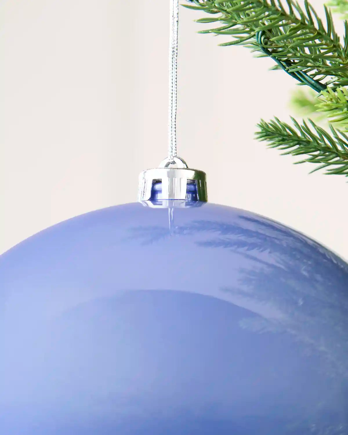 Close up of an Oversized shiny ice blue bauble hanging on a Christmas tree against a cream background