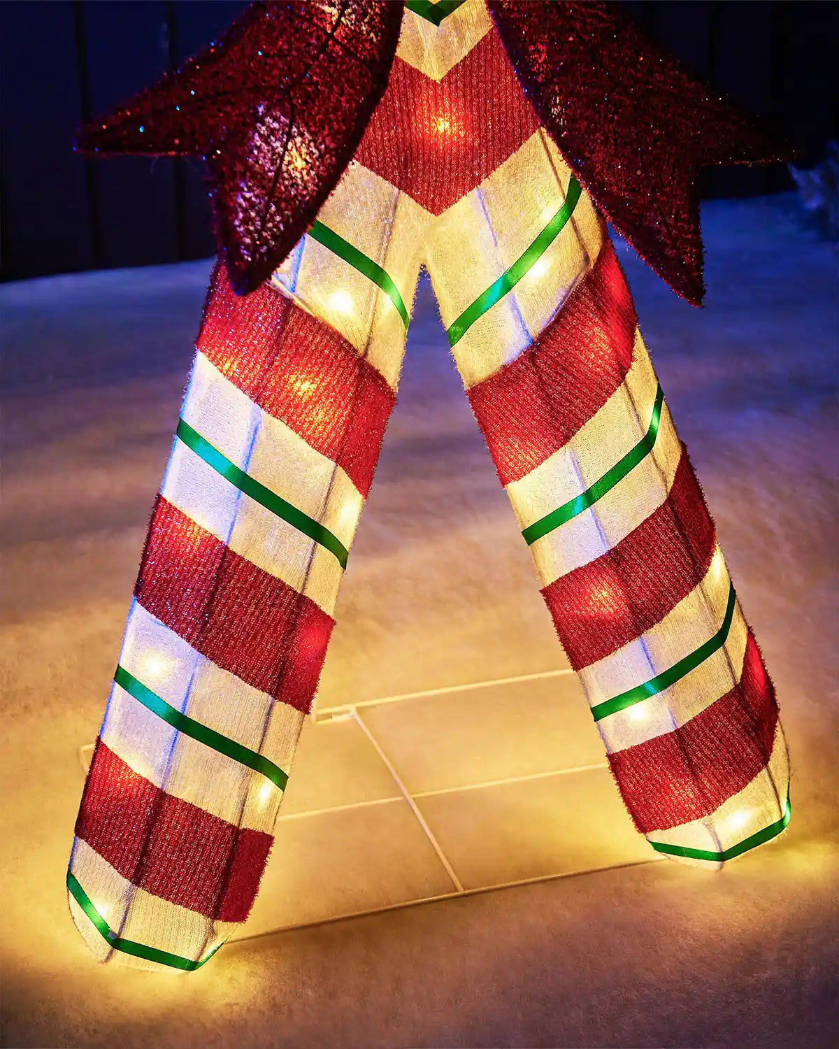 Close up of bottom of LED White and red candy cane with a bow on a dark background and snowy grass