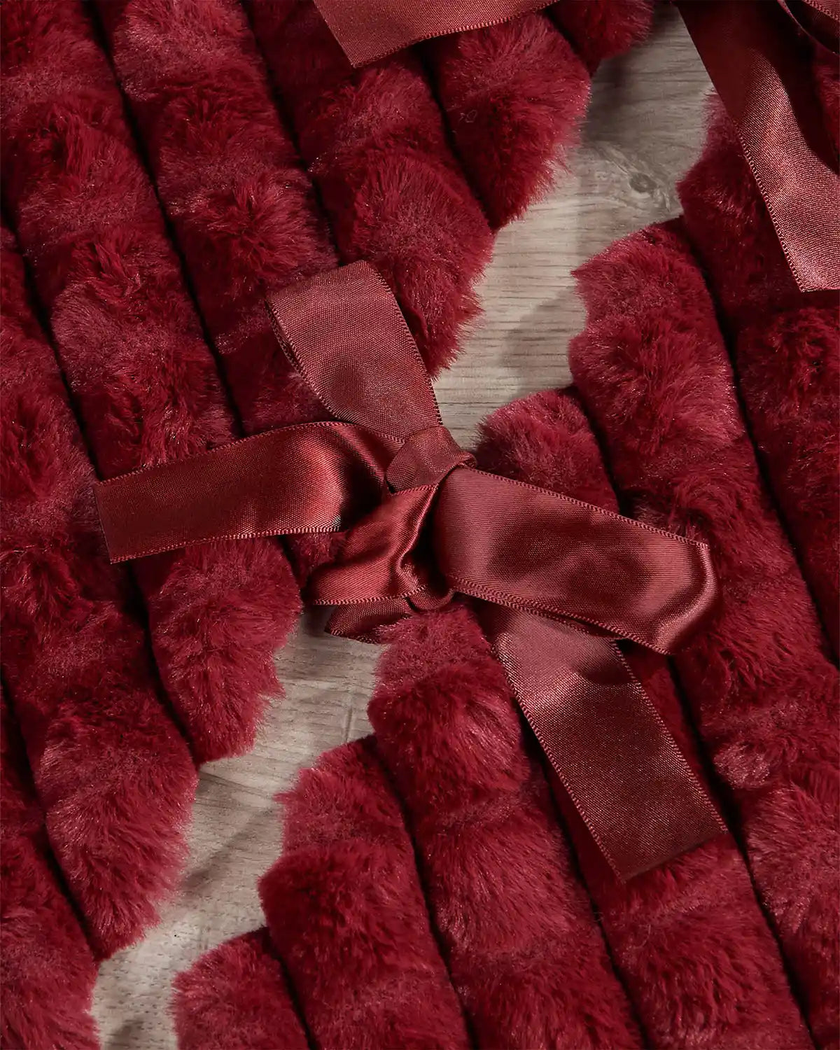 Close-up of burgundy diamond faux fur tree skirt ribbon ties on light wooden flooring