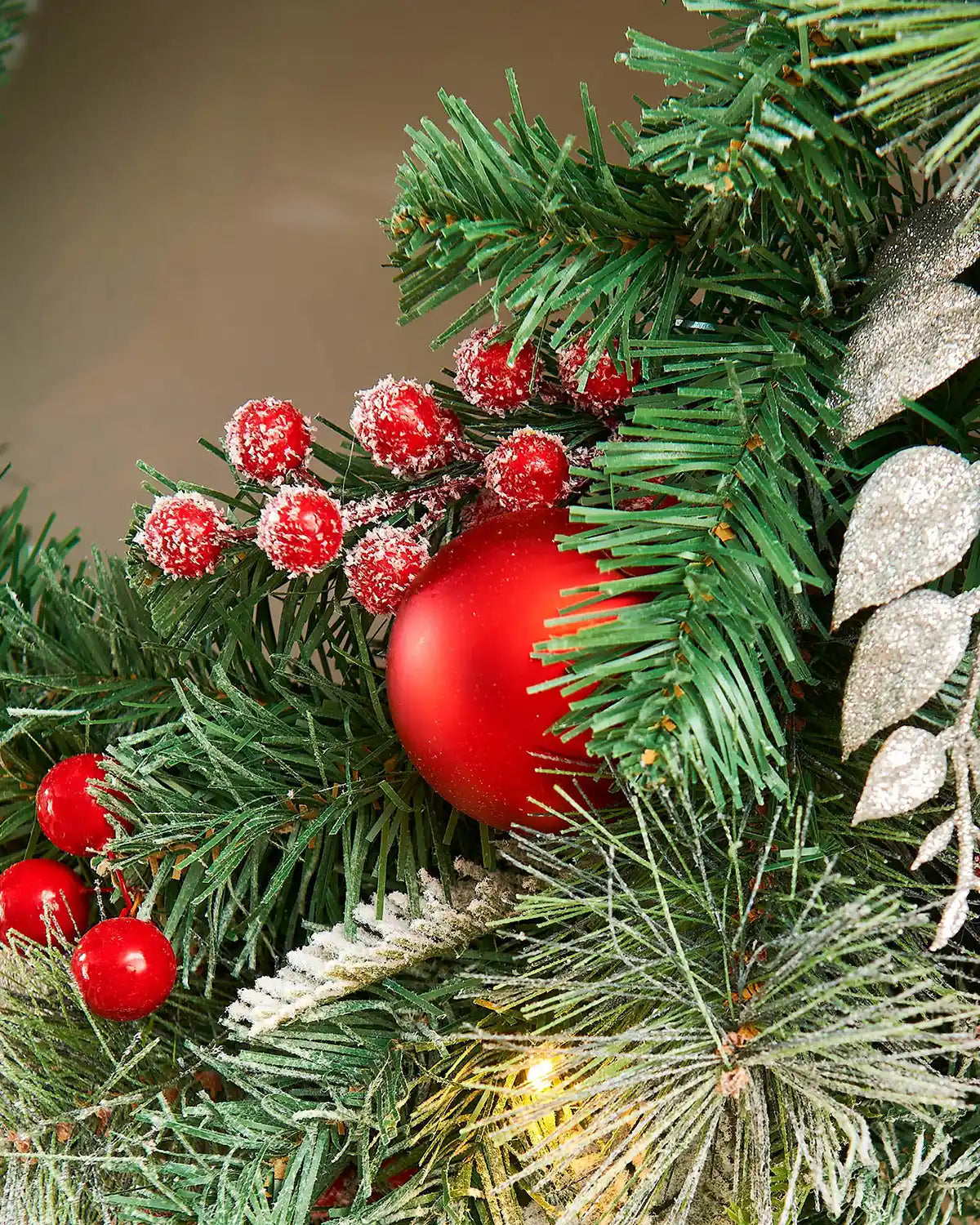 Close up of decorative Christmas wreath with red bauble, berries, and silver leaves on a blurred background