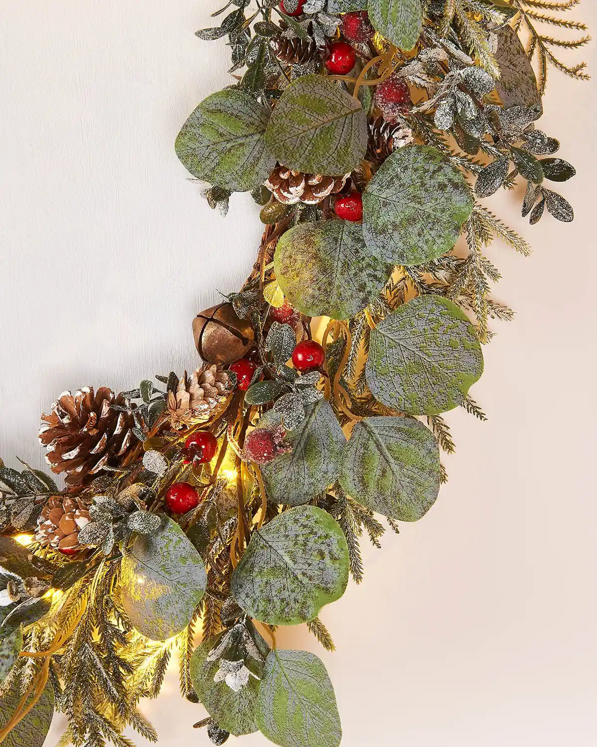 Close up of decorative garland with green leaves, red berries, and gold accents on a white background