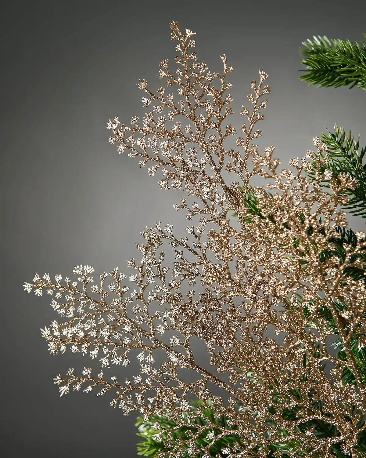 Close up of decorative gold glitter artificial plant stem with small branches on a Christmas tree and a grey background