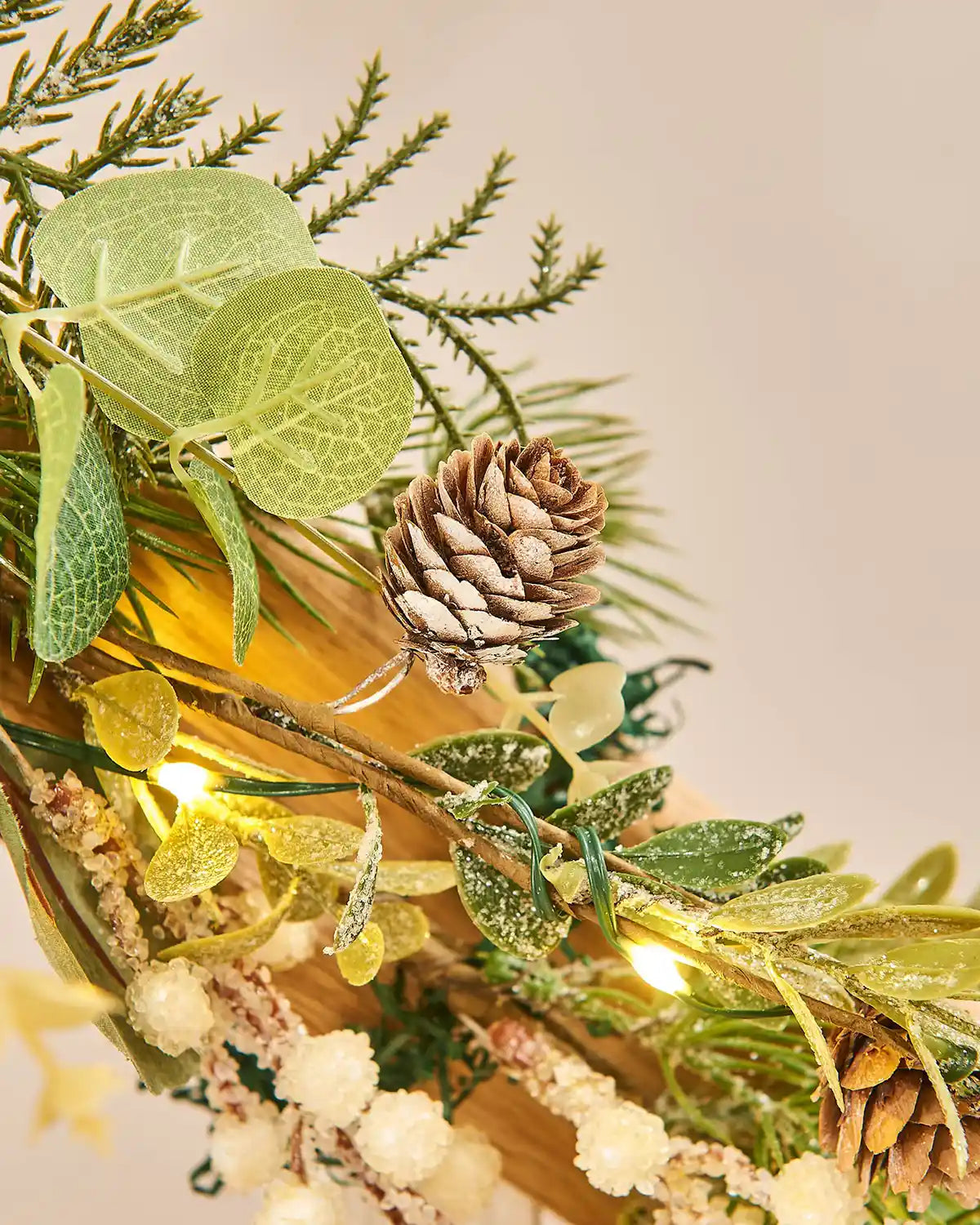 Close up of decorative green wreath and garland with berries pinecones and lights on a staircase banister with a neutral background