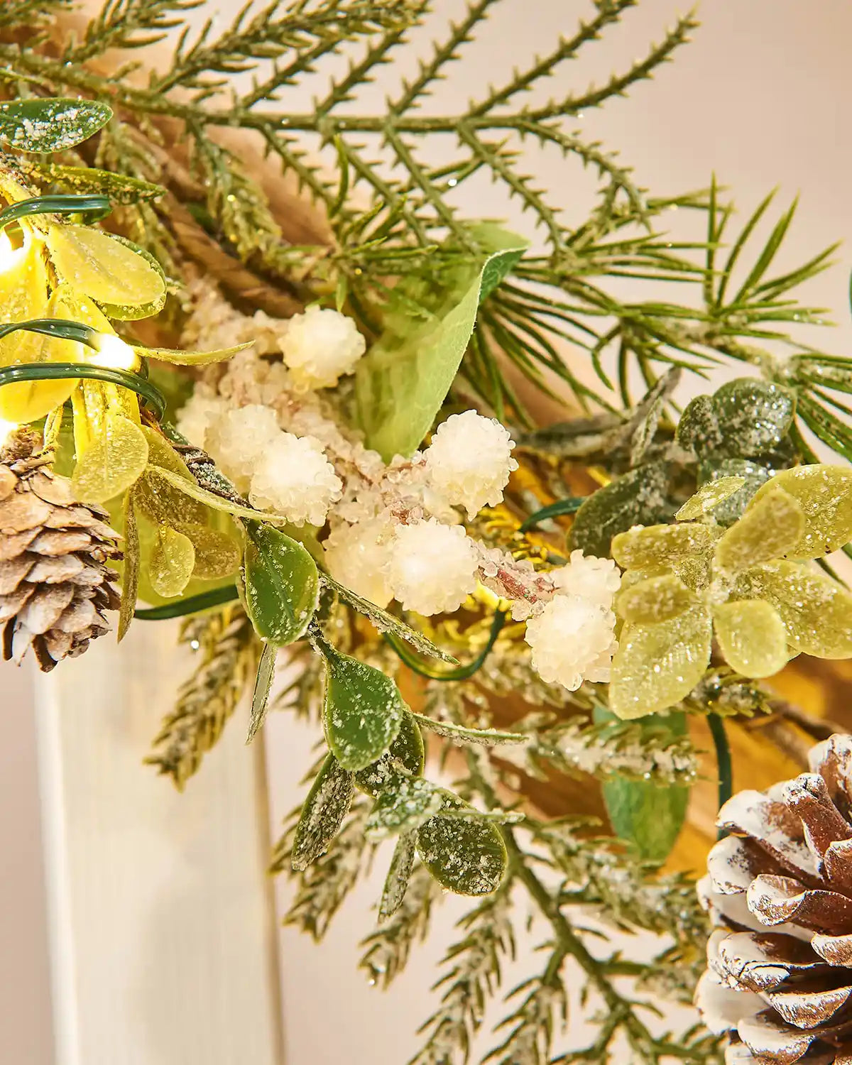 Close up of decorative green wreath and garland with crystalized berries pinecones and lights on a staircase banister with a neutral background