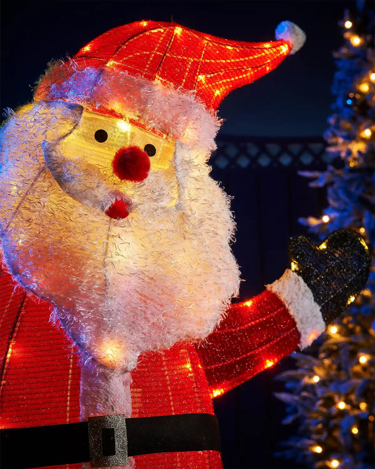 Close up of decorative lighted Santa Claus figure with a tree in the background