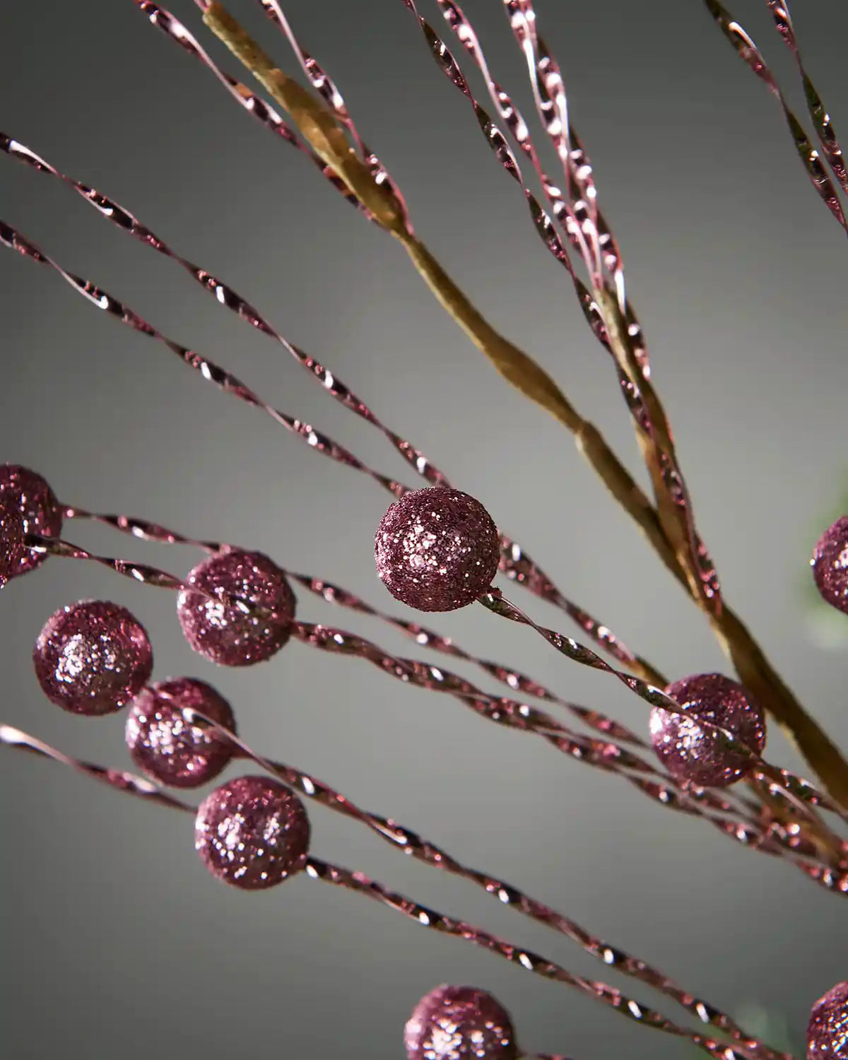 Close up of decorative vine with pink glittery berries on a grey background