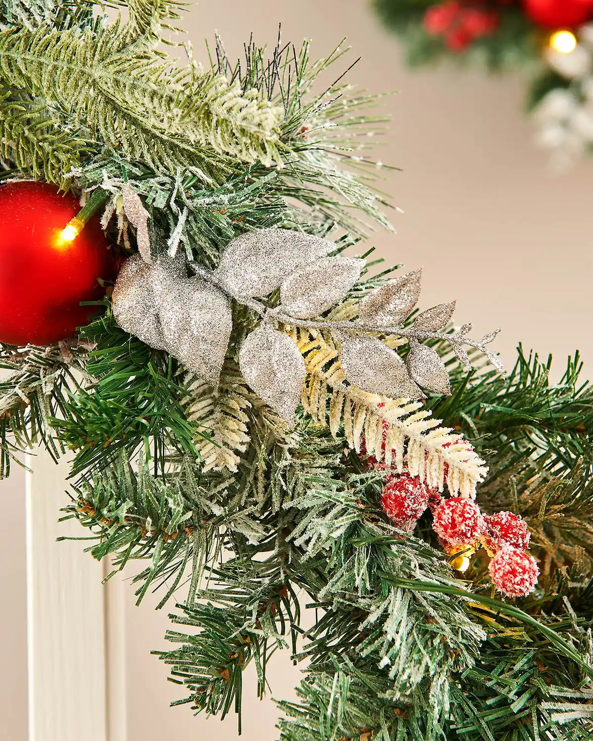 Close-up of green garland with red frosted foliage on white wooden staircase banister 