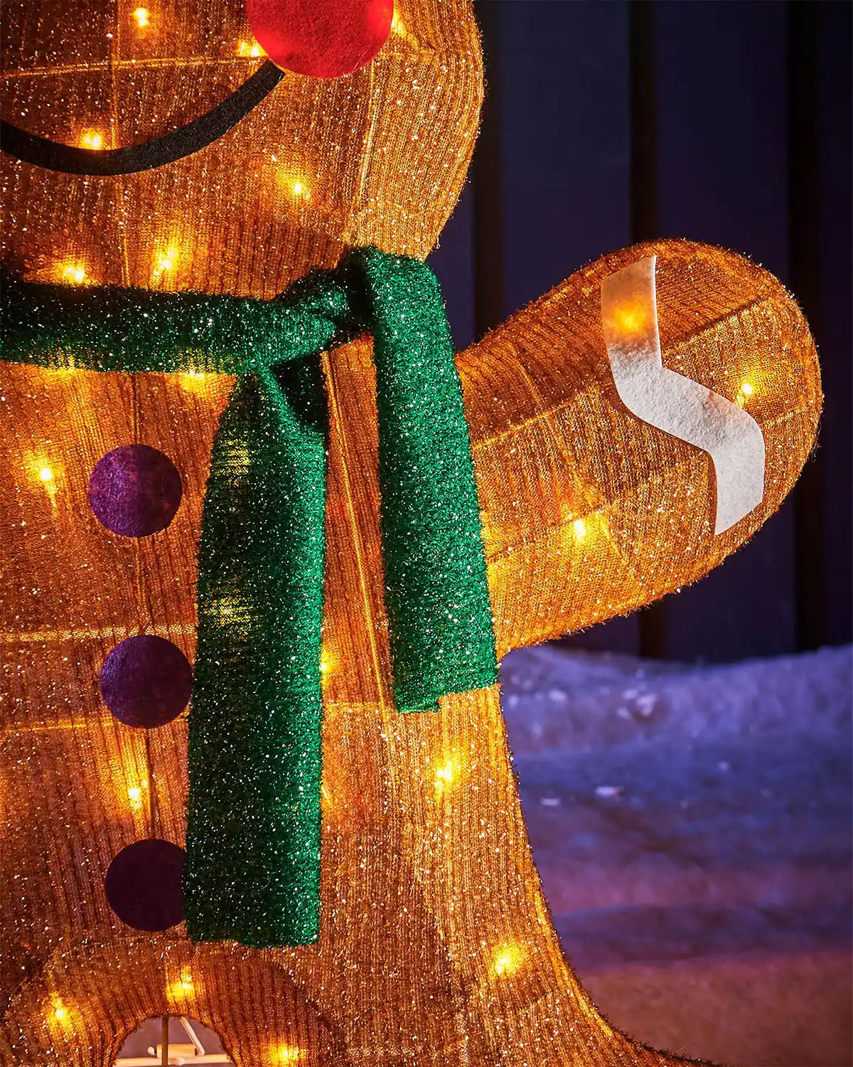 Close up of gingerbread man lights and a green scarf on a dark background